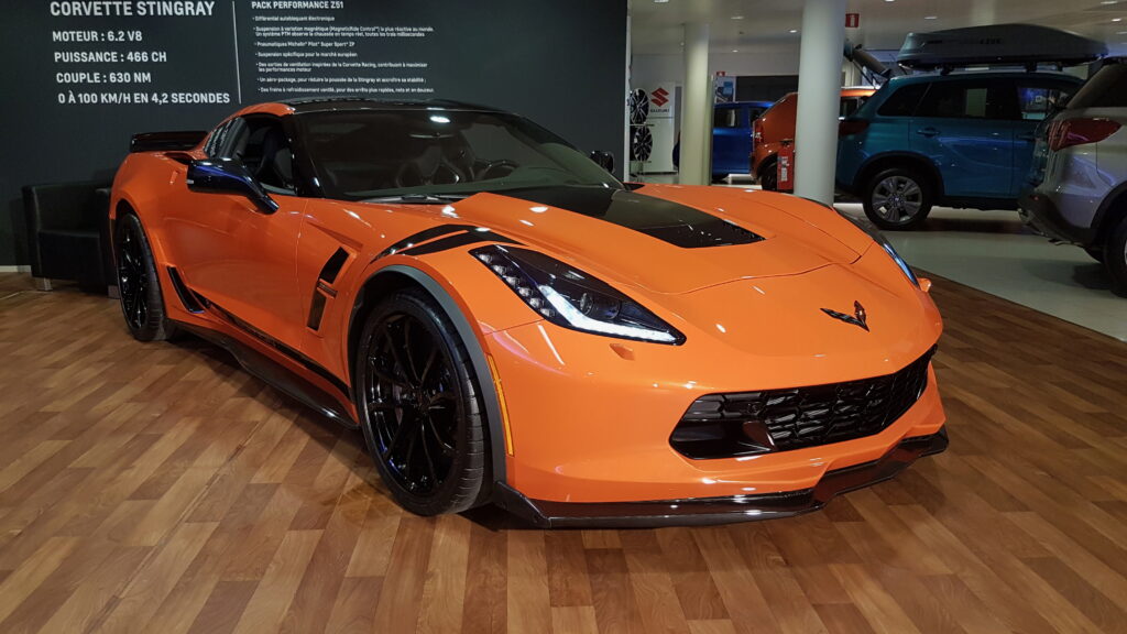 An orange Corvette displayed in the Autopolis showroom, showcasing a luxury performance vehicle.