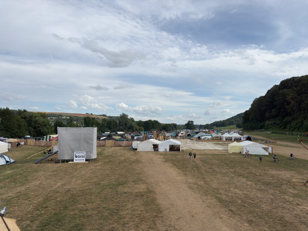 A group of tents set up in a grassy field during a summer camp, surrounded by nature.